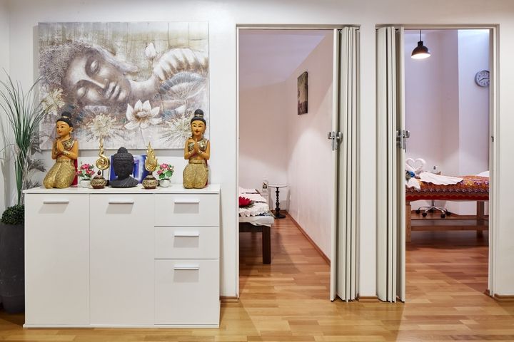 Innenansicht eines Zimmers mit einem weißen Schrank, dekorativen Gegenständen und offenen Türen, die in einen anderen Raum führen.